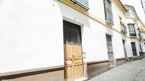Una stretta strada acciottolata con un edificio bianco, una porta in legno e un cancello in metallo.