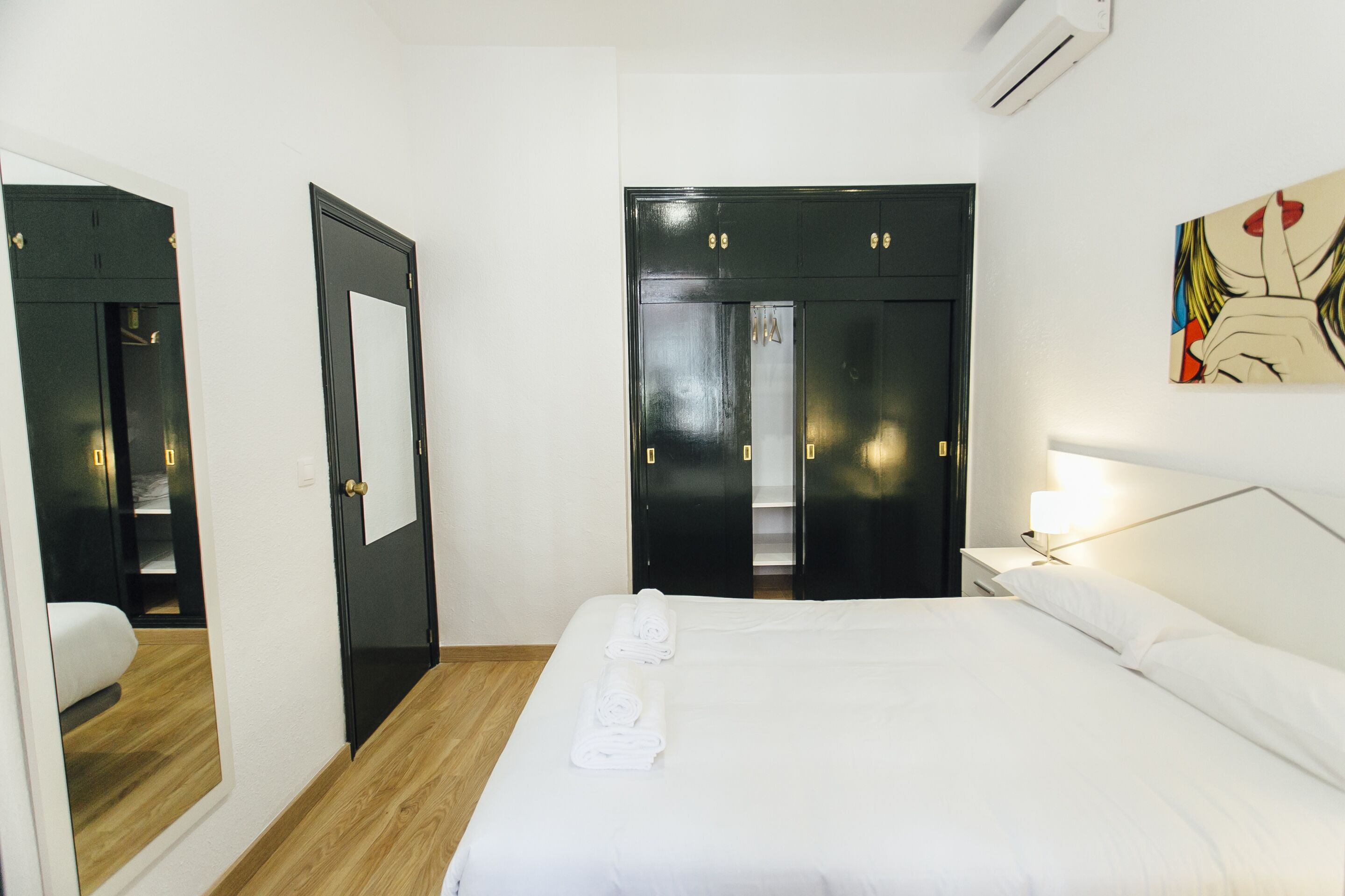 Ein Hotelzimmer mit Bett, Nachttisch, Lampe, Spiegel und Kleiderschrank.