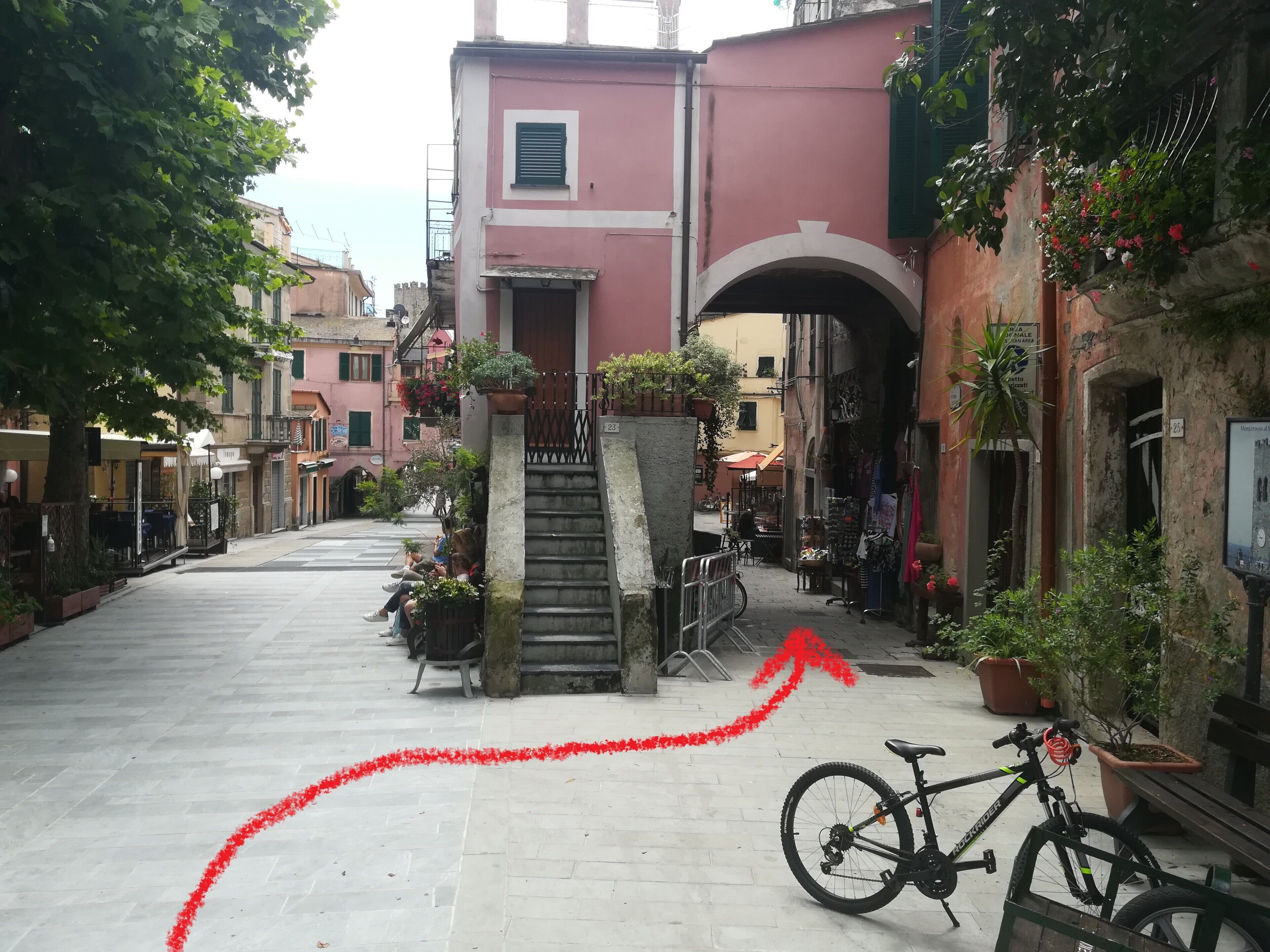 A narrow street with buildings on either side, a bicycle parked on the right, and a staircase leading to a door.
