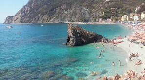 A coastal beach with clear turquoise water, a prominent rock formation, and a crowded beach area with umbrellas and people. - CASA DEL CARUGIO A few steps from the sea, in the middle of historic center (Monterosso al Mare)