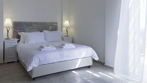 Un letto rifatto con lenzuola e asciugamani bianchi, due lampade ai comodini, una testiera decorativa e un'ampia finestra con tende trasparenti.