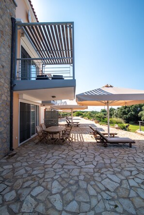 Un patio de piedra con mobiliario exterior, un espacio de estar cubierto y vistas del paisaje circundante.