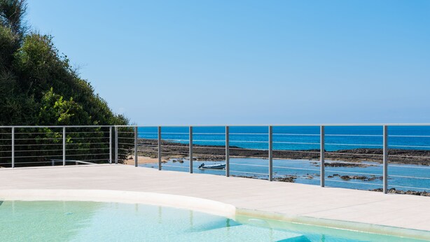 Una piscina con acqua cristallina e gradini che conducono a una spiaggia con ringhiera.
