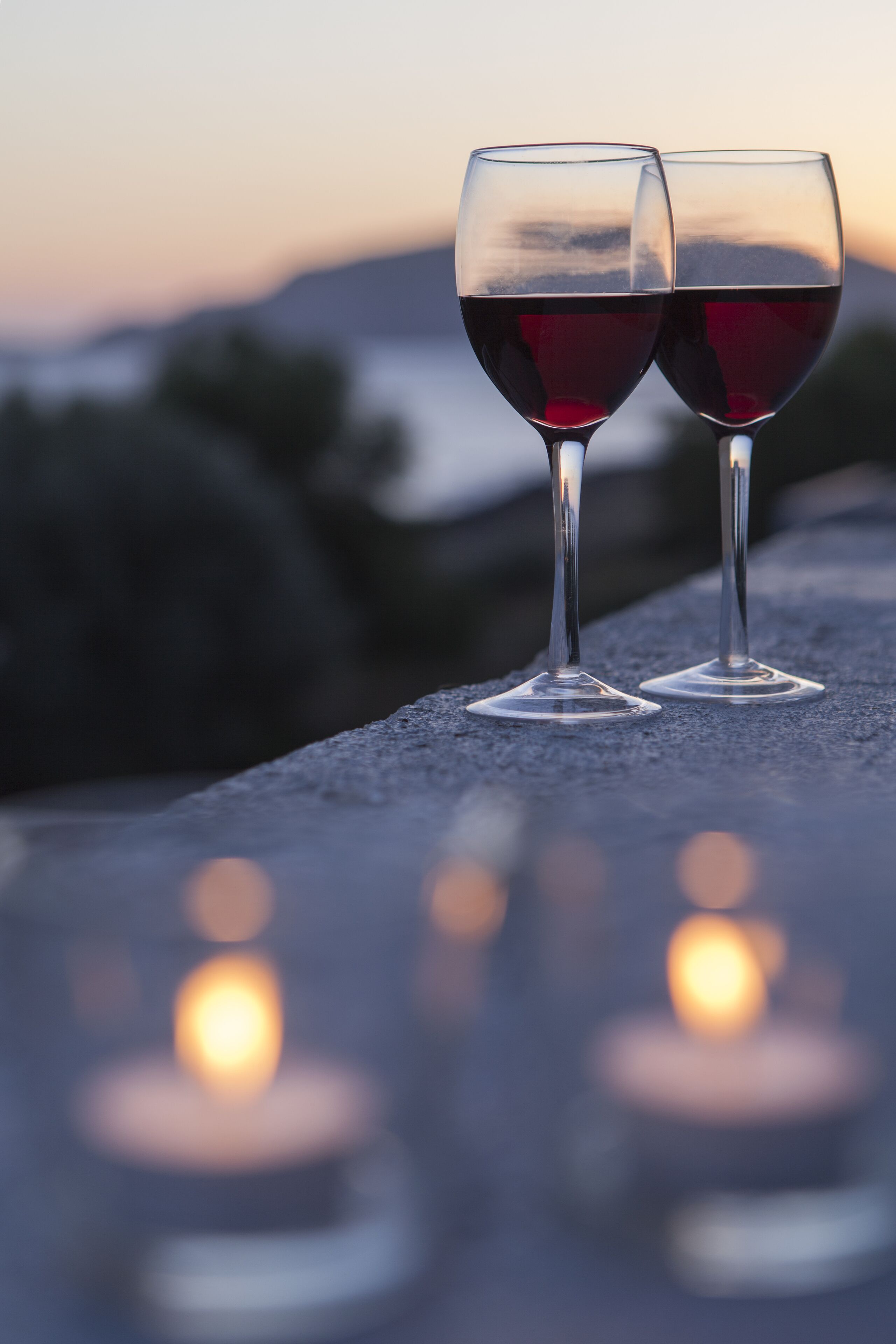 Two wine glasses on a reflective surface with a blurred sunset in the background.