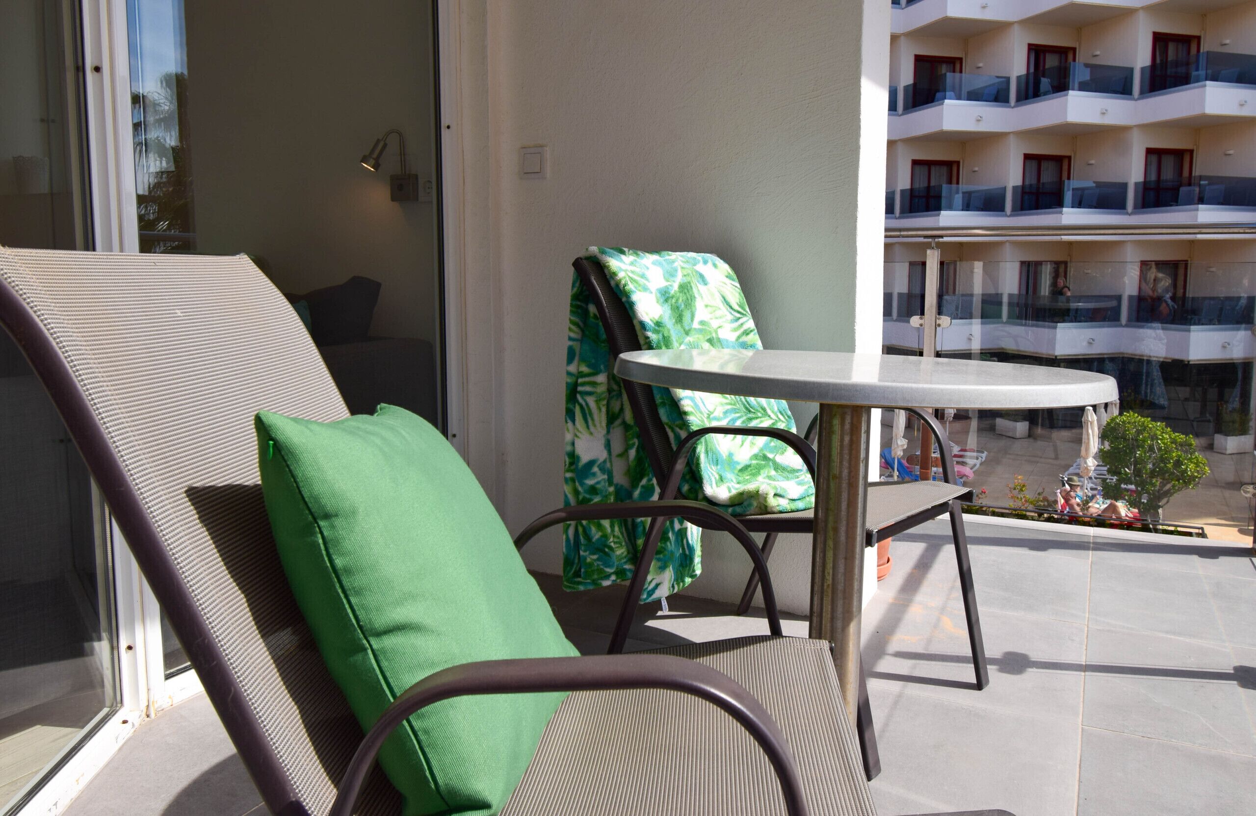 Ein Balkon mit Stuhl und Tisch, Blick auf ein Gebäude mit Balkonen und eine kleine Pflanze.