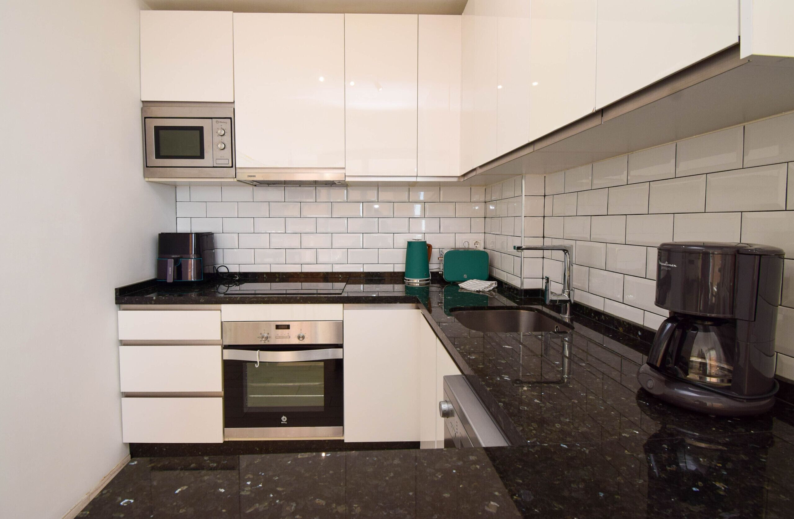 Una cocina moderna con armarios blancos, microondas, cafetera y lavavajillas.