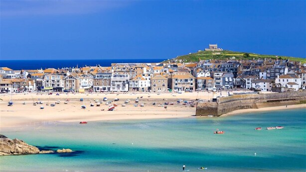 A coastal town with a sandy beach, boats, and a hilltop structure.