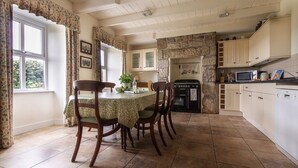 A dining area with a table set for four, surrounded by chairs. There is a stone wall and a kitchen area with cabinets and appliances.