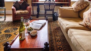 A living room with a sofa, armchair, wooden coffee table, and a patterned rug. There are two windows with curtains, a lamp, and a television.