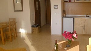 A small kitchen with a refrigerator, a sink, and a countertop. There is a dining area with a table and chairs.