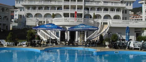 Una gran piscina con un edificio blanco al fondo, que cuenta con varios balcones y una escalera central.