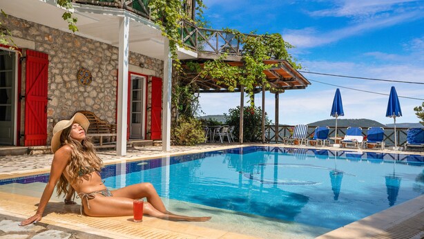 A poolside area with a stone building, red shutters, and a view of the hills. - A HOME FROM HOME! Large stone Villa with pool & stunning views - FREE meal out! (Lefkada)