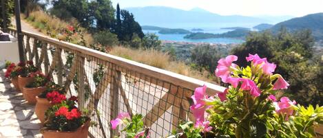 Un balcon agrémenté de pots de fleurs et offrant une vue sur un paysage côtier avec des montagnes.