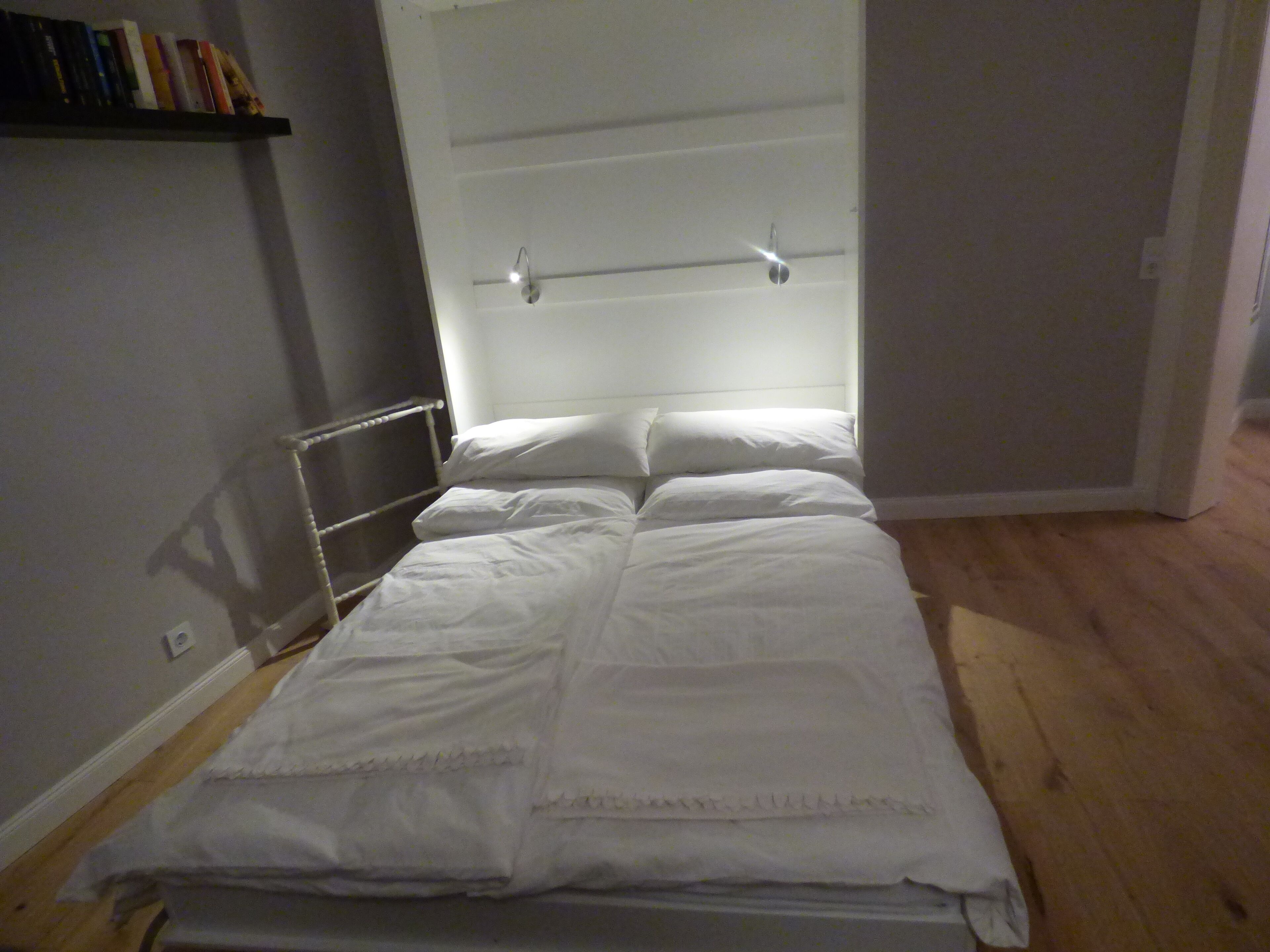 A bedroom with a bed, a radiator, a door, and a shelf with books.