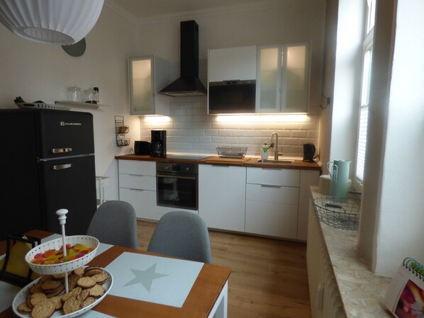 A compact kitchen with white cabinets, a black range hood, and a wooden countertop. - Heidi's favorite place (Eckernförde)