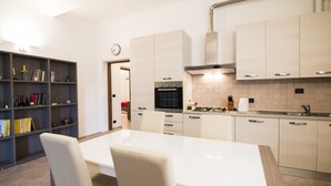 A modern kitchen with a dining area, featuring a white table, chairs, a bookshelf, and a clock on the wall. - Cozy apartment in the historic heart of Piombino (Piombino)