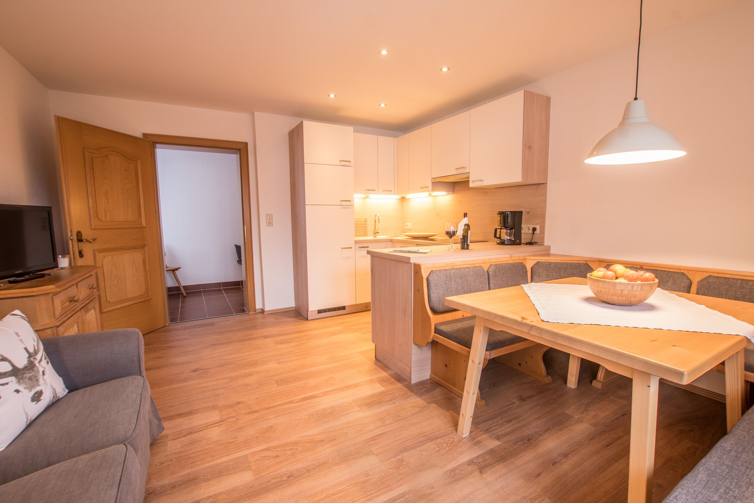A modern kitchen with white cabinets, a wooden dining table, and a built-in bench.