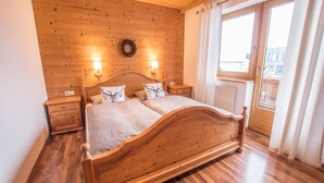 Ein Bett mit Holzrahmen, zwei Nachttische, eine Wandleuchte und ein Blick ins Freie durch ein Fenster.