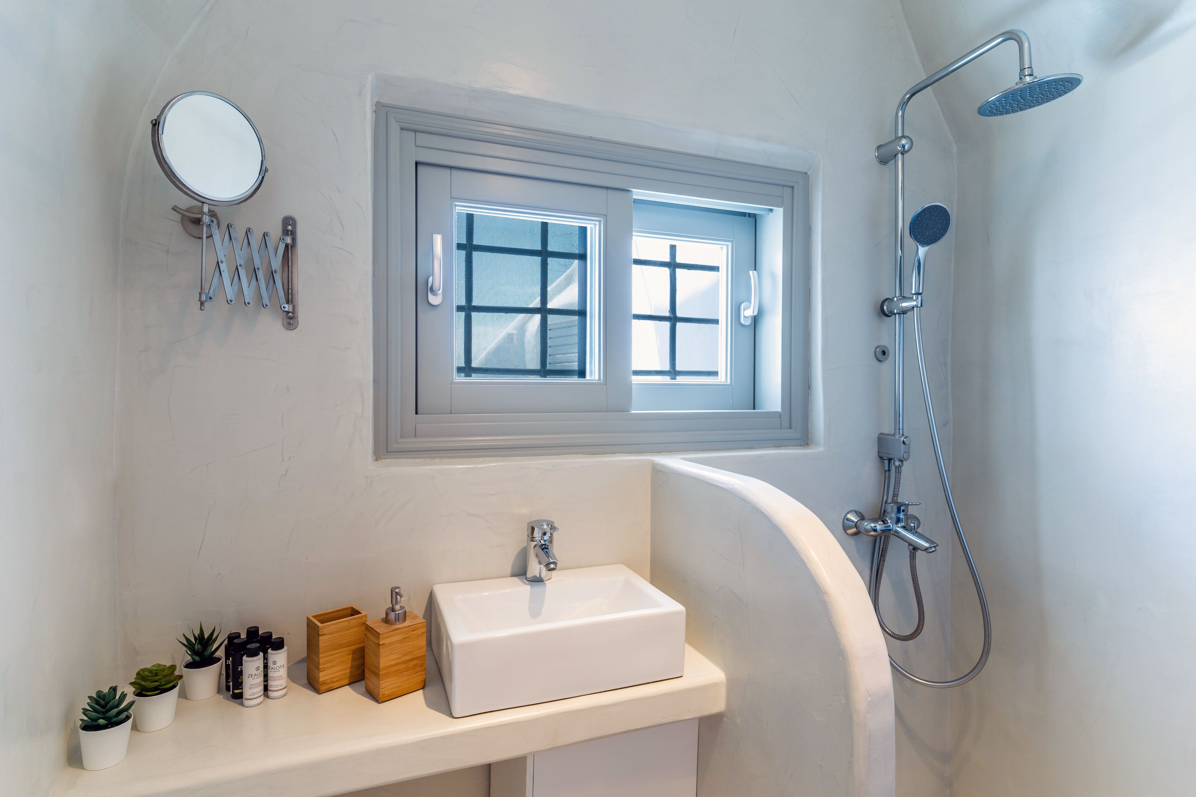 A bathroom with a white sink, a mirror, a window, and a shower.
