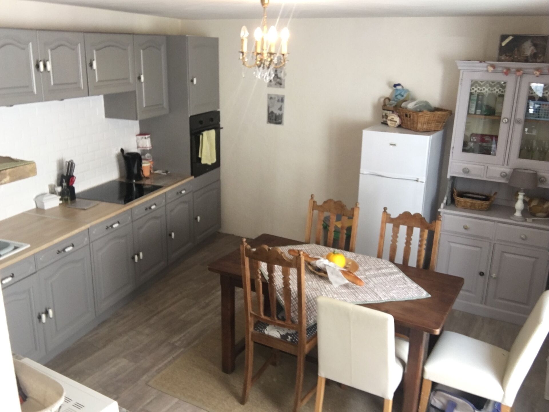 A kitchen with grey cabinets, a white refrigerator, a dining table with chairs, and a chandelier.