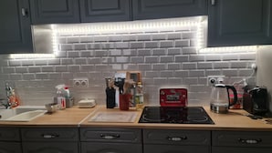 Eine Küche mit weiß gefliester Spritzschutzwand, dunklen Schränken und einer Arbeitsplatte mit verschiedenen Küchenutensilien und Geräten.