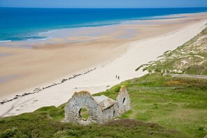 Un paysage côtier avec une plage de sable, une ruine en pierre et une vue dégagée sur l’océan.