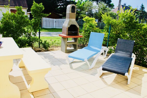 Een terras buiten met twee loungezetels, een tafel en een barbecue van natuursteen.
