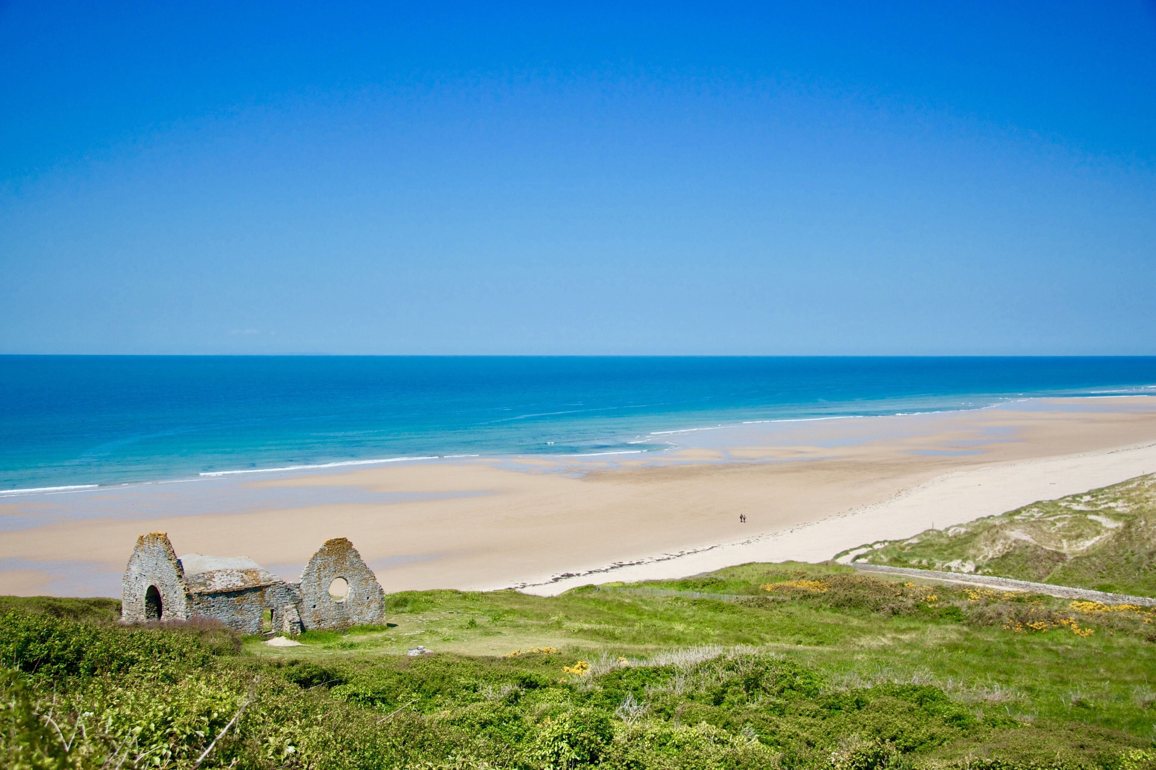 Un paysage côtier avec une plage, une structure en pierre et un ciel bleu dégagé.