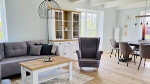 Ein modernes Wohnzimmer mit grauem Sofa, einem Holztisch, einem grauen Sessel und einem Essbereich mit Tisch und Stühlen.