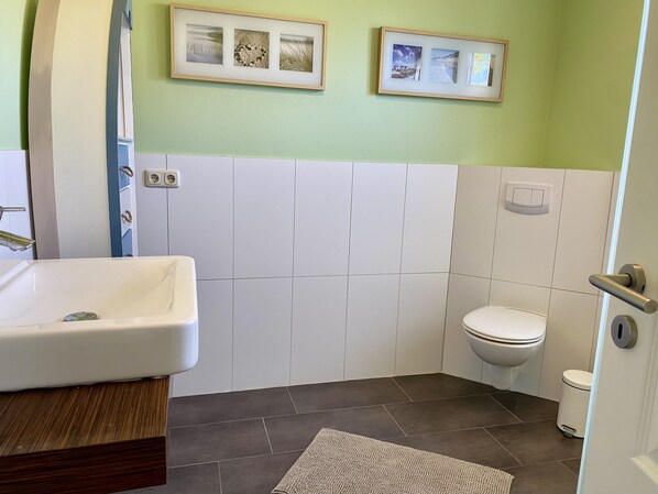 A bathroom with a sink, toilet, and two framed pictures on the wall.