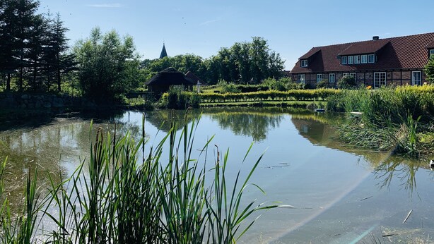 Eine friedliche Flusslandschaft mit einem traditionellen Haus und einem Kirchturm im Hintergrund.