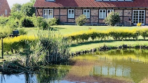 Ein großes Haus mit rotem Dach, einem Teich und einem gepflegten Garten.