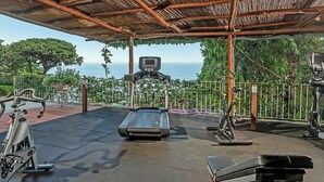 Une salle de sport en plein air équipée de matériel d’exercice, d’un téléviseur et offrant une vue sur la mer.
