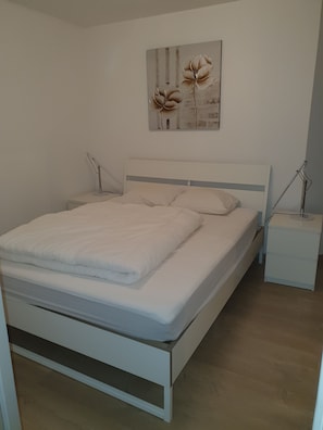 A neatly made bed with white bedding, a headboard, and two bedside tables with lamps.