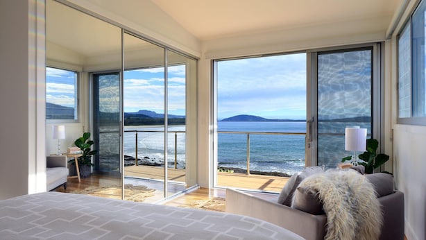 Een slaapkamer met een grote schuifdeur die leidt naar een balkon met uitzicht op zee en bergen.