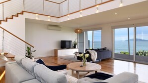 Een moderne woonkamer met een trap, een flatscreen televisie en een groot raam met uitzicht op zee.