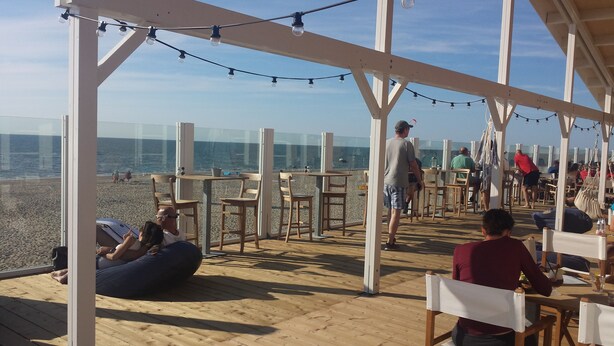 Un espace extérieur aménagé avec des tables et des chaises en bois, donnant sur une plage.