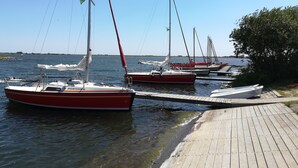 Un port de plaisance où sont amarrés plusieurs voiliers, une jetée en bois et un ciel d’un bleu limpide.