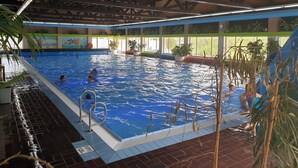 Une piscine intérieure à l’eau claire, entourée d’un sol carrelé et dotée d’une échelle métallique.