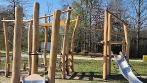 Une aire de jeux avec un toboggan, des structures d’escalade et une cabane en bois.