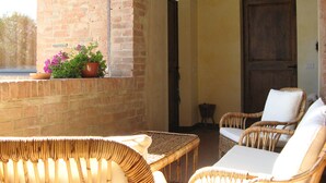 Une terrasse ensoleillée, meublée de meubles en osier, avec un mur en briques et une porte en bois.