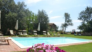 Une piscine entourée de verdure et d’un bâtiment rustique, avec des chaises longues et des parasols à proximité.