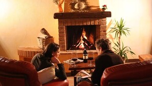 Une pièce chaleureuse avec une cheminée, des fauteuils en cuir et une table sur laquelle se trouvent des verres et une bouteille.
