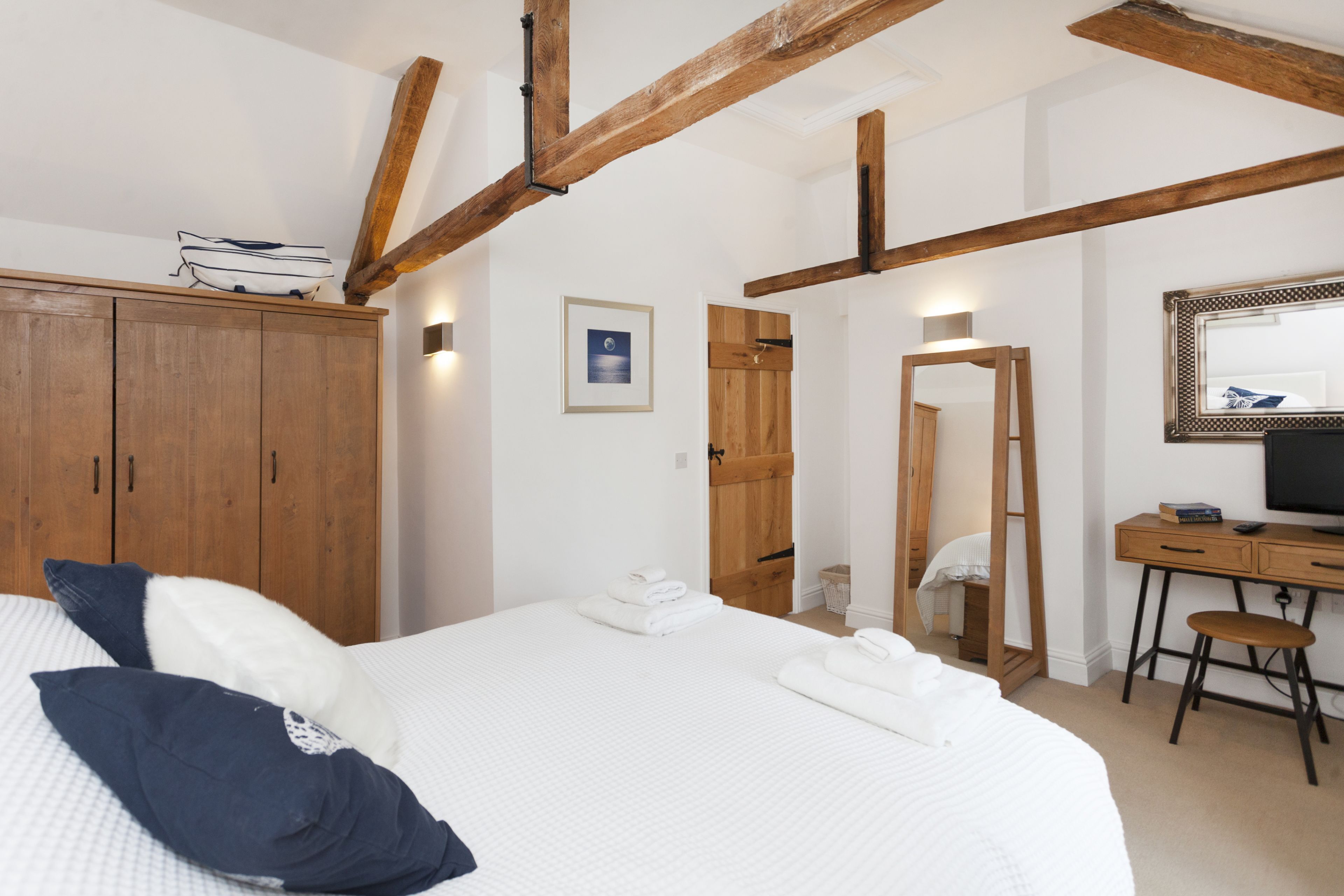 A bedroom with a bed, wooden wardrobe, desk, and a mirror.