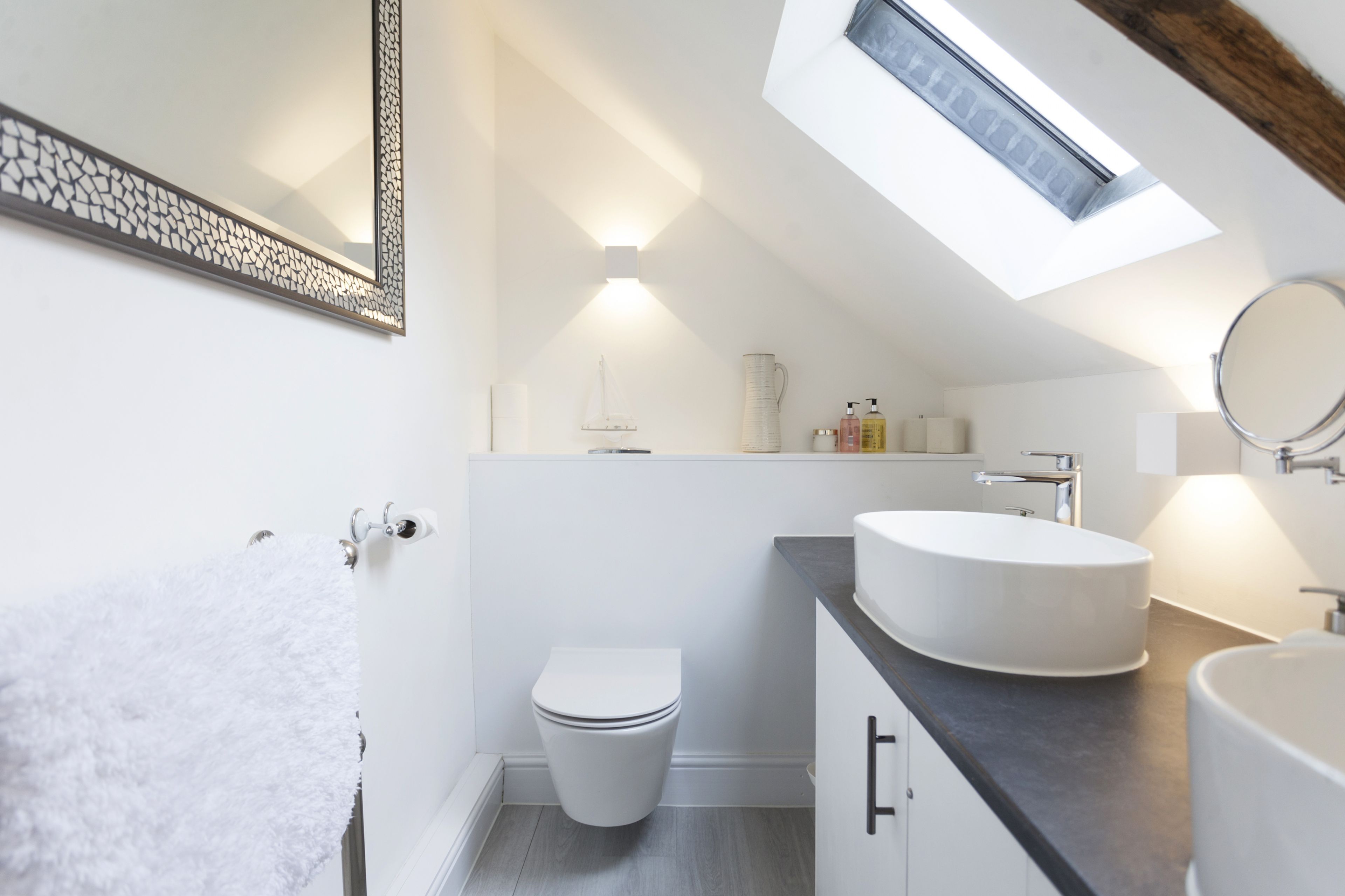 A modern bathroom with a skylight, a white toilet, a round sink, and a towel rack.