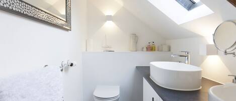 A modern bathroom with a skylight, a white toilet, a round sink, and a towel rack.