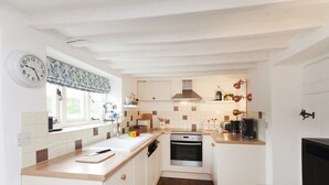 Eine kleine Küche mit weißen Schränken, einer Holz Arbeitsplatte, einem eingebauten Ofen und einem Fenster mit einem gemusterten Vorhang.