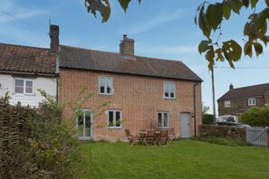 A brick house with a tiled roof, a small garden, and a table with chairs.
