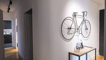 Un pasillo con suelo de madera, una bicicleta colgada en la pared y una mesa con una cesta.