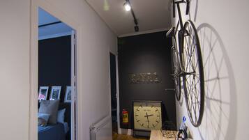 A narrow hallway with a bicycle mounted on the wall, a clock, and a radiator.